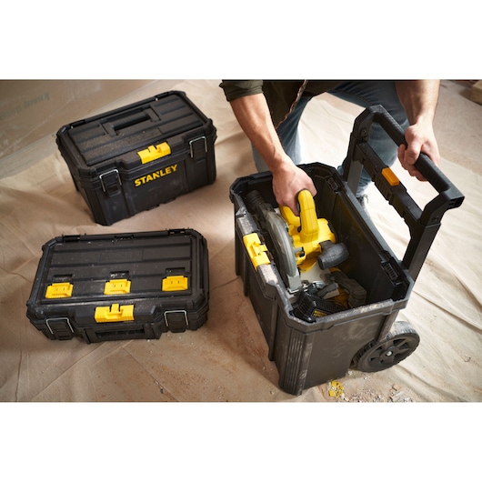 STANLEY STST60500 black rolling tool box with yellow latches, shown with tools and other tool boxes on floor.