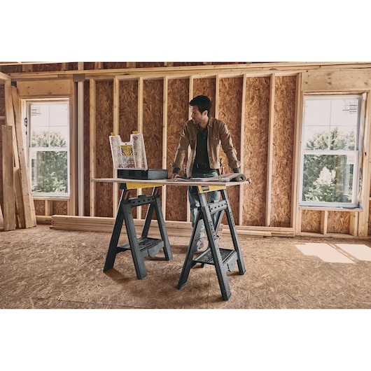 STANLEY STST60626 sawhorse set supports a work surface in a construction room, with tools and plans on top.