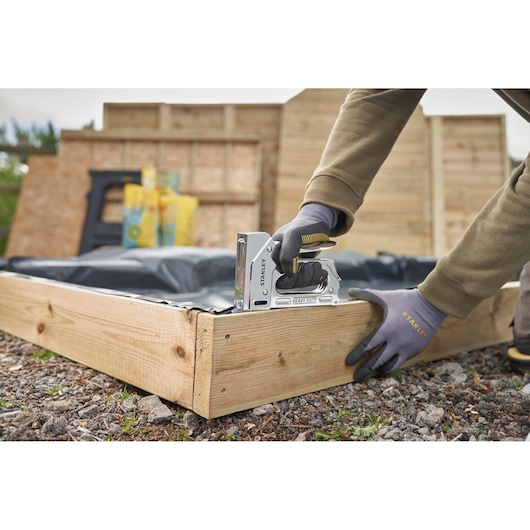 STANLEY TR110 heavy duty staple gun in use securing plastic to a wooden garden frame outdoors.