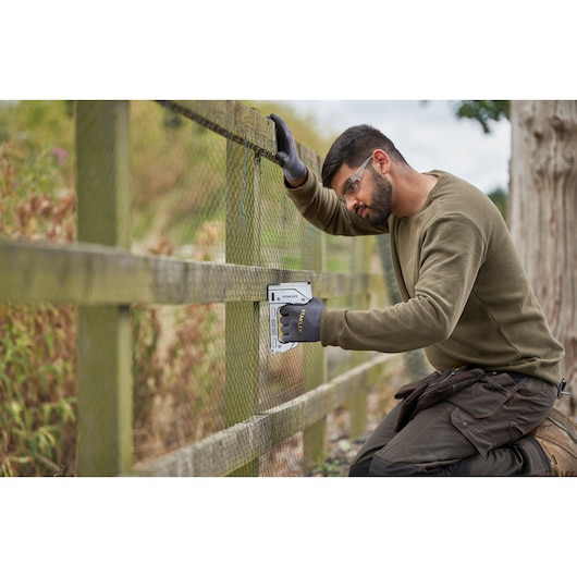Stanley TR110 staple gun used to attach wire mesh to wooden fence outdoors.