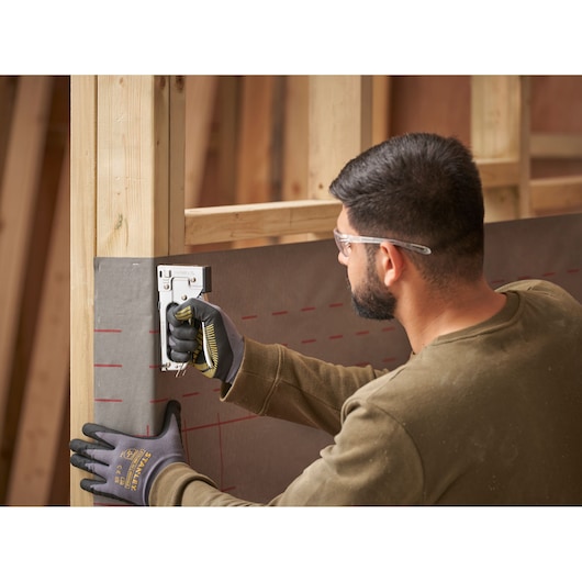 Photo of STANLEY TR45 staple gun in use, person wearing gloves staples sheeting to wooden frame.