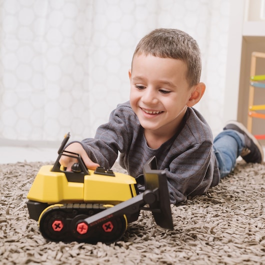 STANLEY TT005-SY photography of yellow toy bulldozer on carpet, child in background playing indoors.
